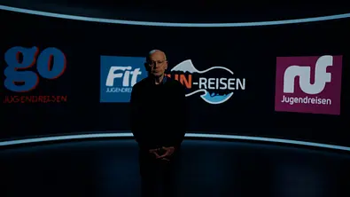 Günther Wallraff steht in einem dunklen Studio vor einer gebogenen Wand mit Logos von Jugendreiseanbietern. - Foto: RTL Günther Wallraff steht in einem dunklen Studio vor einer gebogenen Wand mit Logos von Jugendreiseanbietern. - Foto: RTL