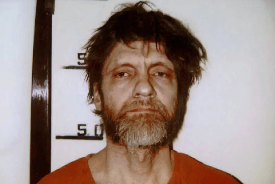 Ted Kaczynski hielt auch im Gefängnis noch gerne philosophische Vorträge. Ted Kaczynski steht im April 1996 mit zerzaustem Haar, grauem Vollbart und orangefarbenem Oberteil vor einer Größenmessskala.