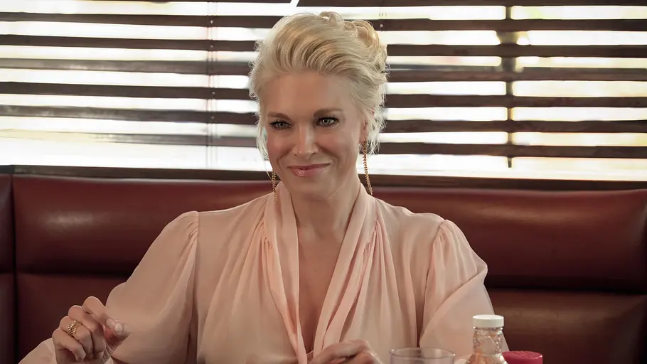 Rebecca Welton sitzt in einem Dinner und schaut lächelnd nach vorne.