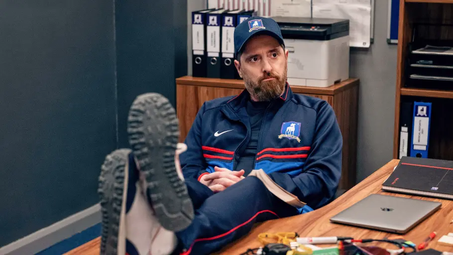 Coach Beard hat die Füße auf dem Tisch und schaut zur Seite.