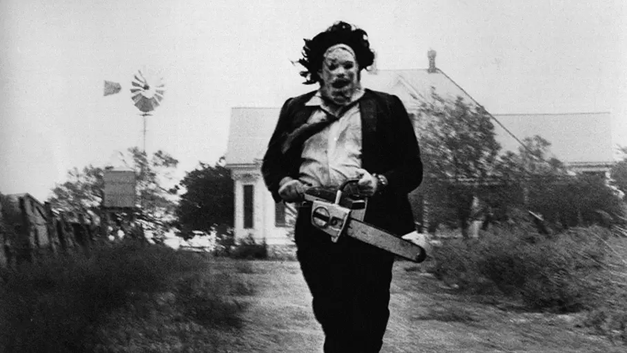 Texas Chainsaw Massacre Leatherface rennt mit einer Kettensäge auf einem Feldweg. Hinter ihm ist ein Haus.