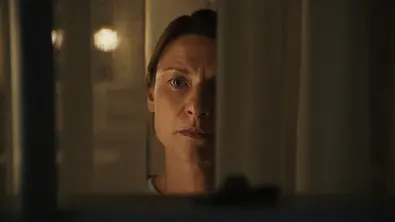 Aggie Wiggs steht am Fenster und schaut zwischen ihren Gardinen nach Draußen. - Foto: Netflix