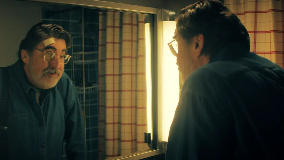 The Boroughs Alfred Molina schaut sich selbst ratlos im Spiegel ein.