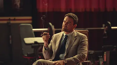 Theo James raucht in The Gentleman eine Zigarre und sitzt auf einem Stuhl - Foto: Netflix Theo James raucht in The Gentleman eine Zigarre und sitzt auf einem Stuhl - Foto: Netflix