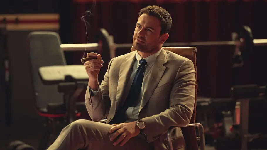 The Gentleman Theo James Theo James raucht in The Gentleman eine Zigarre und sitzt auf einem Stuhl