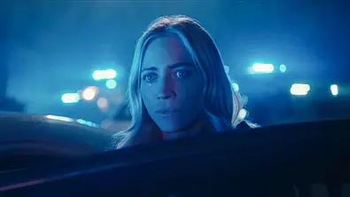 Brittany Snow blickt als Sophie hinter einer Autotür hervor. Blaues Licht beleuchtet ihr Gesicht, im Hintergrund leuchten Blaulichter. - Foto: Netflix Brittany Snow blickt als Sophie hinter einer Autotür hervor. Blaues Licht beleuchtet ihr Gesicht, im Hintergrund leuchten Blaulichter. - Foto: Netflix