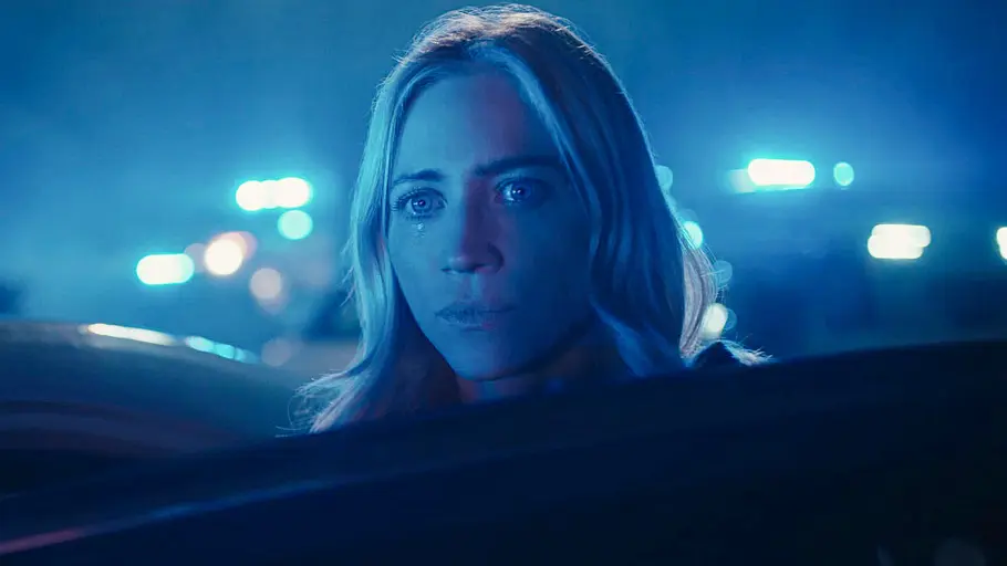 Staffel 2 von „The Hunting Wives“ kommt noch dieses Jahr zu Netflix. Brittany Snow blickt als Sophie hinter einer Autotür hervor. Blaues Licht beleuchtet ihr Gesicht, im Hintergrund leuchten Blaulichter.