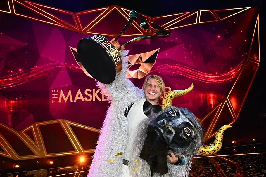Vincent Gross gewinnt als Fernando El Toro Vincent Gross hält lächelnd einen Pokal hoch und trägt eine gehörnte Tiermaske im Arm. Er steckt in einem weißen Fellkostüm.