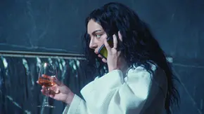 Charli XCX steht mit einem Weinglas in der Hand in einem Badezimmer und telefoniert. Im Weinglas ist Aperol Spritz.  - Foto: Universal