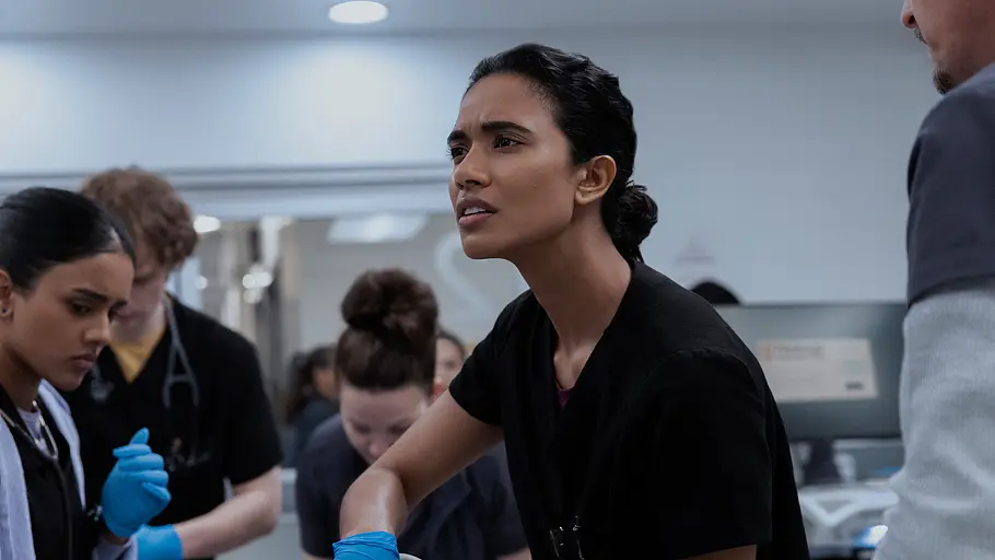 The Pitt Eine Ärztin in schwarzer OP-Kleidung koordiniert konzentriert die Versorgung eines Notfallpatienten, während ein medizinisches Team im Hintergrund zusammenarbeitet – Szene aus der Krankenhausserie „The Pitt“.