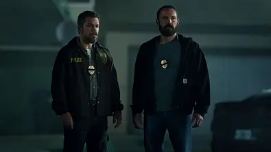 Matt Damon (l.) und Ben Affleck stehen in Cop-Montur in einer Tiefgarage. - Foto: Netflix