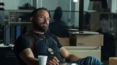 Detective Sergeant J.D. Byrne im T-Shirt und Jeans. Er trägt eine Polizeimarke und schaut sein Gegenüber emotionslos an. - Foto: Claire Folger/Netflix