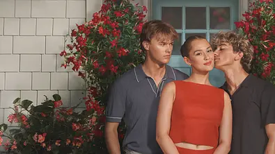 Conrad, Belly und Jeremiah stehen vor einem Haus. Belly lächelt, Jeremiah küsst ihre Wange und Conrad schaut seinen Bruder voller Wut an.  - Foto: Prime Video