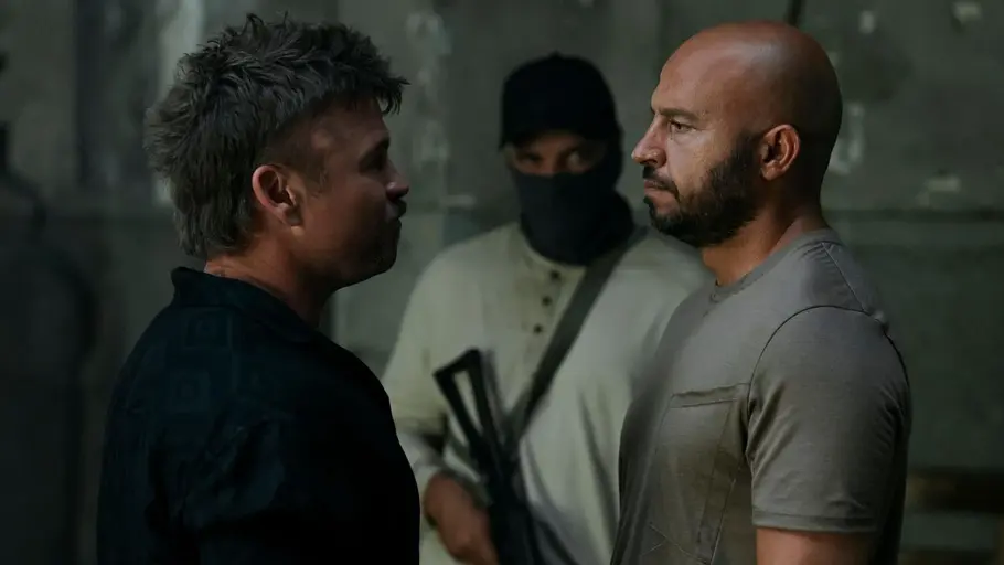 „The Terminal List“ Staffel 2: Die Verschwörung wird persönlich Jules Landry und Mohammed Farooq stehen sich gegenüber. Hinter ihnen steht eine vermummte Person mit einem Gewehr.
