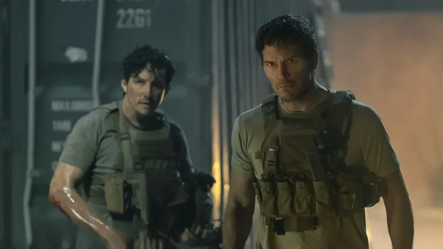 „The Terminal List“ Staffel 2: Showdown im Finale Freddy Strain und James Reece stehen in taktischen Westen vor Containern. Der Mann links hält eine Waffe und hat Blut am Arm.