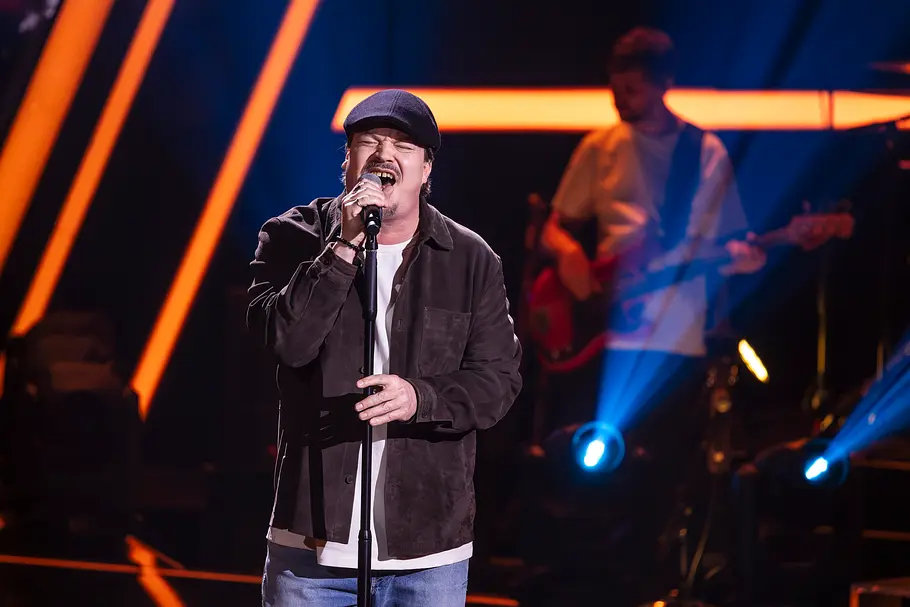 The Voice Folge 4 Tommy Morgenstern Tommy Morgenstern singt auf der Bühne von The Voice. Er trägt eine dunkelblaue Kappe und ei