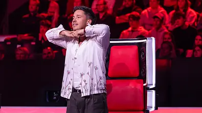 Nico Santos steht im weißen Hemd vor einem roten Jurystuhl und hält die Hände unter dem Kinn. Im Hintergrund sitzt Publikum. - Foto: Joyn Nico Santos steht im weißen Hemd vor einem roten Jurystuhl und hält die Hände unter dem Kinn. Im Hintergrund sitzt Publikum. - Foto: Joyn