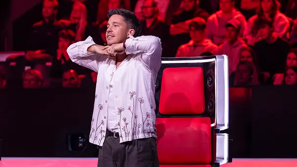 Nico Santos steht im weißen Hemd vor einem roten Jurystuhl und hält die Hände unter dem Kinn. Im Hintergrund sitzt Publikum. - Foto: Joyn Nico Santos steht im weißen Hemd vor einem roten Jurystuhl und hält die Hände unter dem Kinn. Im Hintergrund sitzt Publikum. - Foto: Joyn
