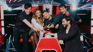 Die Coaches von „The Voice Kids“ sitzen gemeinsam auf den roten Stühlen im Studio und legen ihre Hände übereinander - Foto: Joyn/Christoph Köstlin