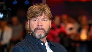 Rea Garvey trägt eine dunkle Jeansjacke über einem weißen Shirt. Im Hintergrund sind unscharf mehrere Personen zu sehen. - Foto: IMAGO / STAR-MEDIA Rea Garvey trägt eine dunkle Jeansjacke über einem weißen Shirt. Im Hintergrund sind unscharf mehrere Personen zu sehen. - Foto: IMAGO / STAR-MEDIA