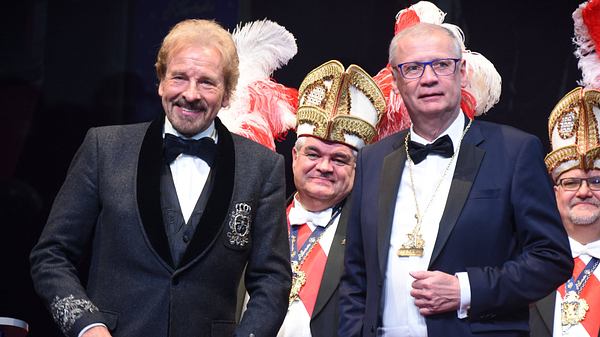 Man sieht Gottschalk und Jauch in zwei Anzügen auf einer Art Karnevalsveranstaltung. Hinter ihnen stehen Personen in entsprechenden Aufzügen. - Foto:  IMAGO / Lindenthaler