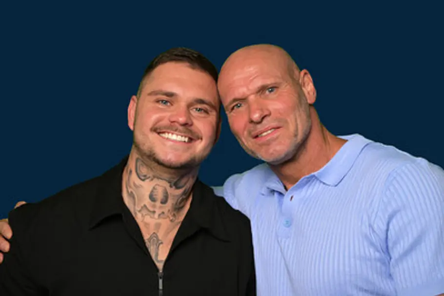 Thorsten und Nico Legat stehen lächelnd vor dunkelblauem Hintergrund, einer in Schwarz, der andere in einem hellblauen Poloshirt.
