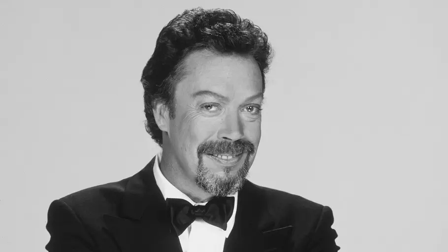 Tim Curry Tim Curry lächelt verwegen in die Kamera. Er trägt einen Anzug mit Fliege.