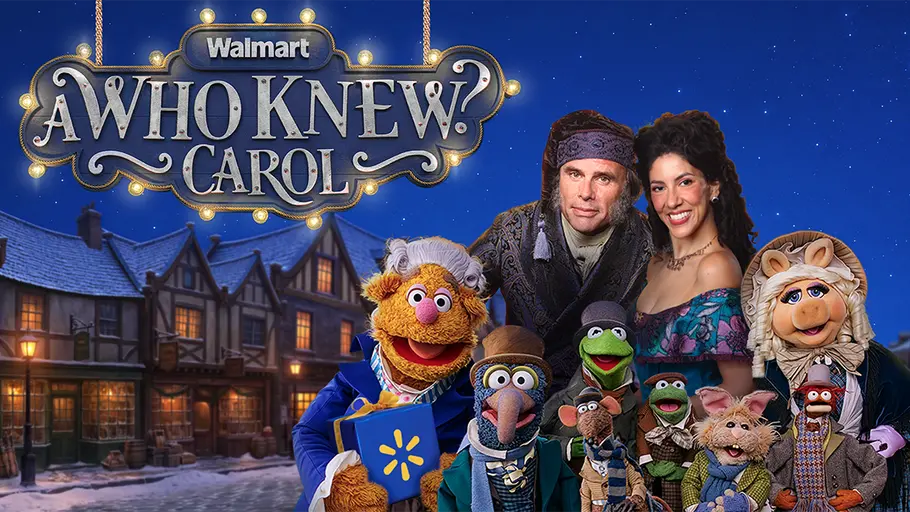 Tiny Tim ist natürlich auch wieder mit dabei! Ein Mann, eine Frau und Muppets posieren vor einer verschneiten Häuserkulisse unter dem Schriftzug „Walmart – A Who Knew? Carol“.