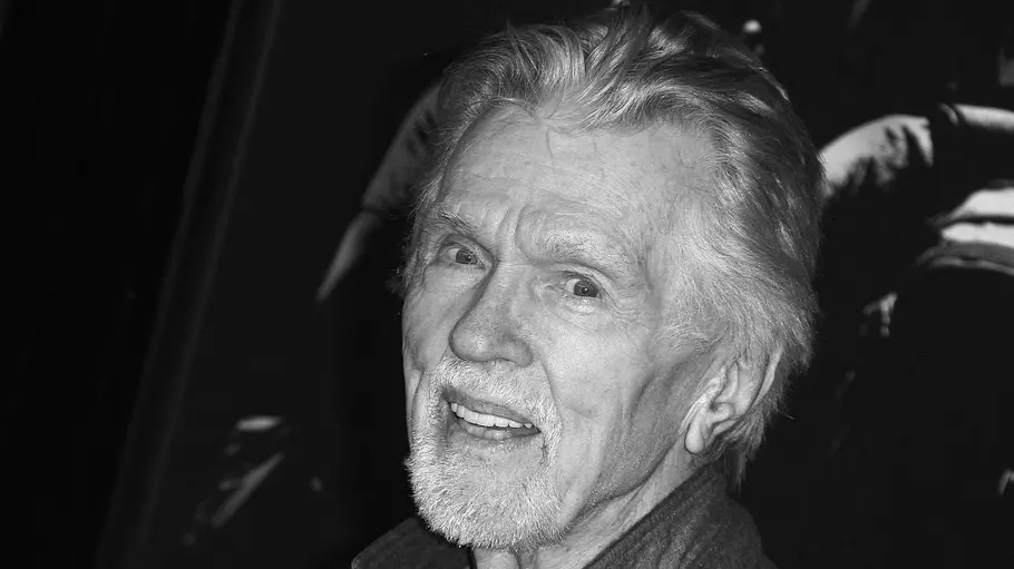 Tom Skerritt stand auch im hohen Alter noch vor der Kamera. Tom Skerritt lächelt mit weißem Kinnbart und zurückgekämmtem Haar in die Kamera. Die Nahaufnahme ist in Schwarz-Weiß.