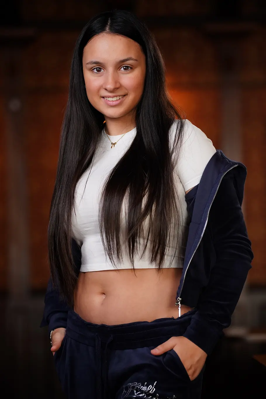 Valentina Wagner Valentina mit langen dunklen Haaren trägt ein weißes Crop-Top und eine dunkle Jacke, lächelt in die Kamera.