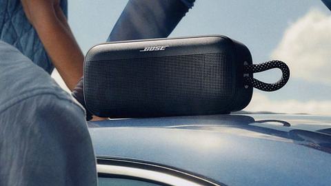 Der neue tragbare Bose SoundLink Plus Lautsprecher in Nahaufnahme steht auf einem Autodach bei Sonnenschein. - Foto: © Bose Corporation 2025