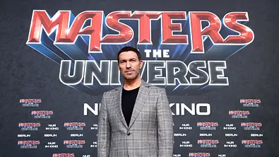 Travis Knight steht im karierten Anzug vor einer großen „Masters of the Universe“-Premierenwand. - Foto: Sebastian Reuter/Getty Images for Sony Pictures Entertainment Deutschland GmbH