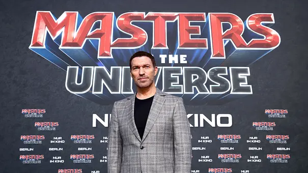 Travis Knight steht im karierten Anzug vor einer großen „Masters of the Universe“-Premierenwand. - Foto: Sebastian Reuter/Getty Images for Sony Pictures Entertainment Deutschland GmbH