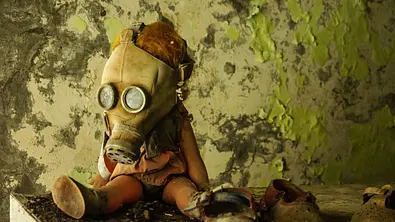 Tschernobyl - Die Katastrophe: Eine Kinderpuppe trägt eine Gasmaske. Sie sitzt vor einer abbröckelnden Tapete auf einer schmutzigen Fläche. Daneben steht ein Paar Kinderschuhe. - Foto: ZDF/Shutterstock