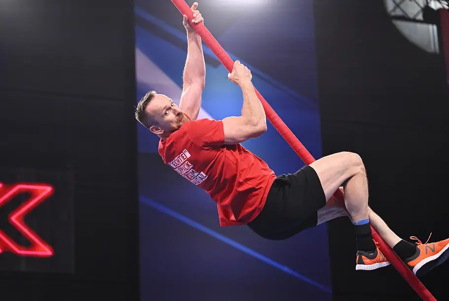Ulrich Wolf ist Teilnehmer bei Ninja Warrior Germany 2026 Ulrich Wolf hält sich mit Händen und Beinen an einer roten Stange fest. Er trägt ein rotes Shirt und schwarze Shorts.