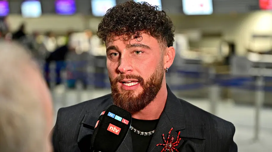 Umut Tekin privat Umut Tekin am 17.01.2026 am Flughafen auf dem Weg ins Dschungelcamp 2026 mit einer Fake-Spinne auf der Jacke und RTL-Mikrofon vor dem Mund.