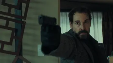 Felix Kramer steht vor einer Wohnwand und richtet eine Schusswaffe nach links. - Foto: Netflix Felix Kramer steht vor einer Wohnwand und richtet eine Schusswaffe nach links. - Foto: Netflix