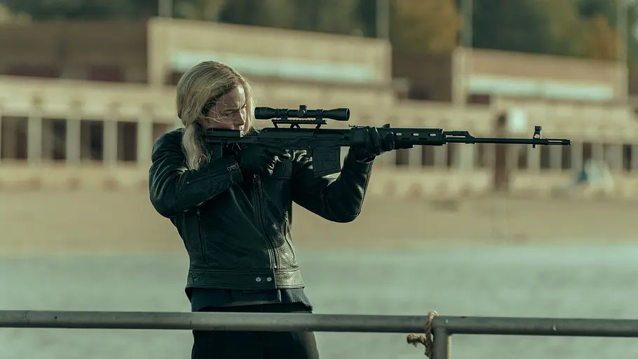 Susanne Wolff steht mit einem Scharfschützengewehr am Wasser. 