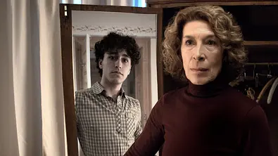 Adele Neuhauser steht vor einem Spiegel. Im Spiegelbild sieht man das Abbild eines jungen Mannes.  - Foto: BR/ORF/Bavaria Fiction GmbH/Jacqueline Krause-Burberg