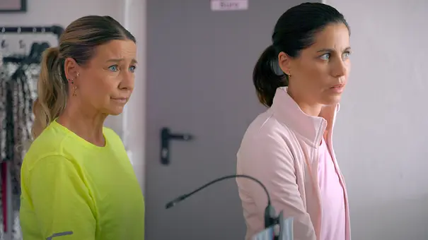 Unter-Uns-Szene: Ute im neongelben Shirt und Sina in einer hellrosa Jacke stehen nebeneinander und blicken ernst nach rechts. - Foto: RTL