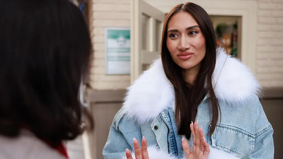 Samira in einer Jeansjacke mit Fell. Sie hält ihre Hände hoch und sieht etwas überfordert aus