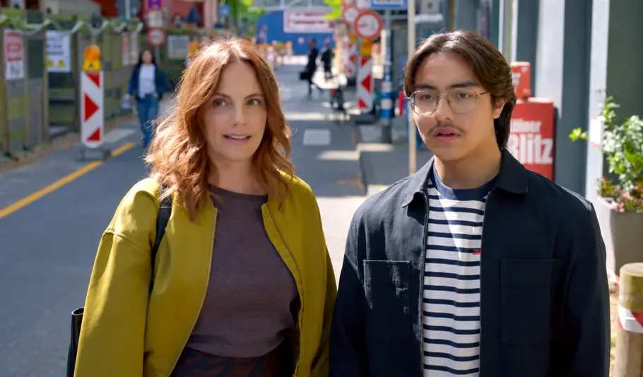 UNTER UNS Vorschau Folge 7986 Tränen lügen doch Annas (Marie Zielcke) in gelbgrüner Jacke und Taro (Cecil Schuster) mit Brille und gestreiftem Shirt stehen nebeneinander auf einer Straße mit Baustellenabsperrungen.
