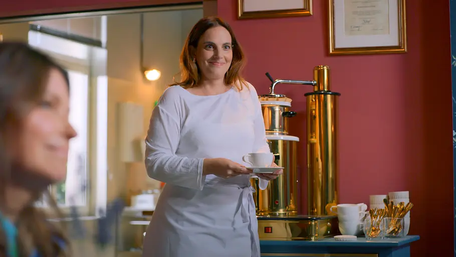 UNTER UNS Vorschau Folge 7987 Die Date-DiebinS Anna (Marie Zielcke) lächelt verschwommen im Vordergrund, Britta (Tabea Heynig, l.) steht mit einer Tasse dahinter.