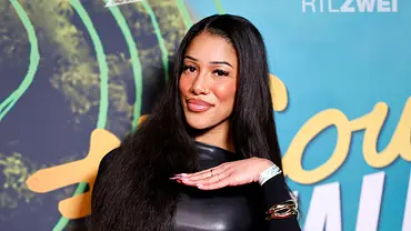 Reality-TV-Teilnehmerin posiert bei einem RTLZWEI-Event vor einer Logo-Wand, trägt ein schwarzes Lederkleid, transparente Strumpfhose mit Herzmuster und hält eine Handtasche. - Foto: IMAGO / Panama Pictures