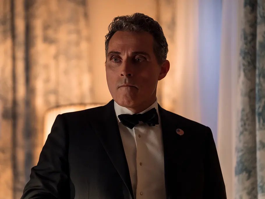 Vermutlich bleibt Hal in seinem Amt, damit die Wylers nicht die Verbindungen zum Weißen Haus verlieren. Rufus Sewell als Hal Wyler trägt einen schwarzen Smoking mit Fliege und US-Flaggenanstecker. Er blickt ernst zur Seite.