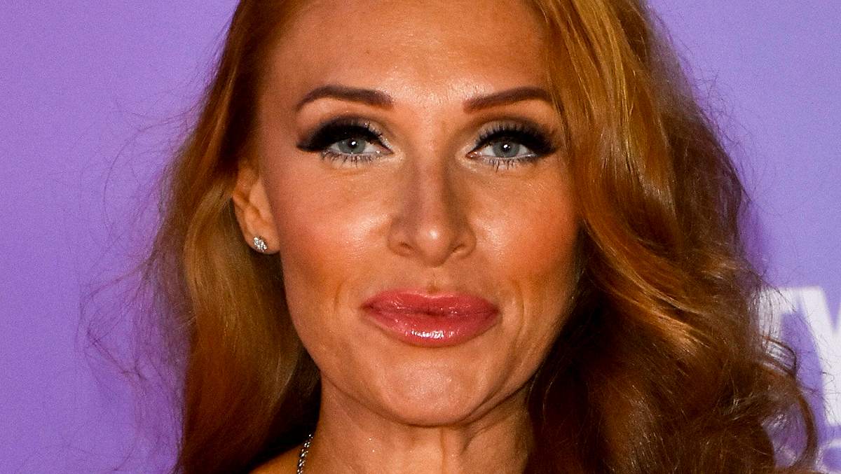 Georgina Fleur, mit offenen Haaren und stark geschminkten Augen, lächelt sanft in die Kamera.