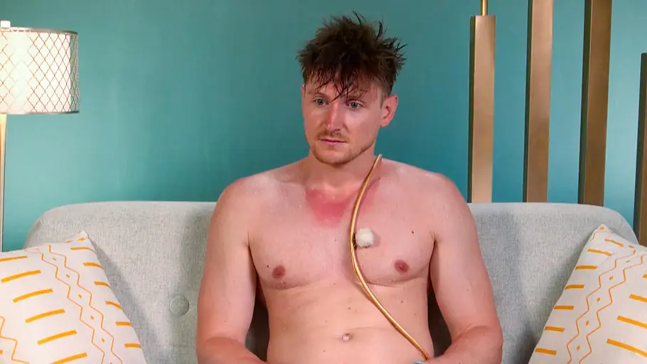 Tommy Pedroni Tommy sitzt im Interview Raum vor einer blauen Wand, er hat nasses, zerzaustes Haar und einen Sonnenbrand auf dem oberen Brustkorb bzw unter dem Hals. Außerdem ist er mit einem Mikro verkabelt, das über seinem Oberkörper hängt.