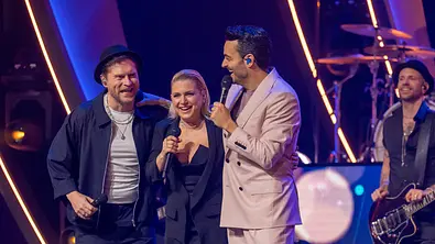 Die Giovanni Zarrella Show - Ein Abend für die Liebe: Johannes Oerding, Jeanette Biedermann und Giovanni Zarrella stehen gemeinsam auf der Bühne. Sie lachen fröhlich. Im Hintergrund steht der Gitarrist der Giovanni-Zarrella-Band. - Foto: ZDF / Sascha Baumann