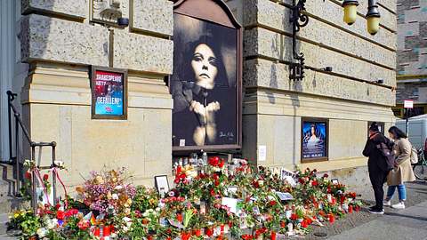 Das Theater des Westens in Berlin. Ein Bild von AnNa R. ziert einen Teil der Wand, auf dem Boden liegen Blumen und Kerzen. - Foto: IMAGO / PEMAX