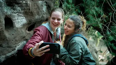 Zwei junge Mädchen stehen im Wald zwischen Felsen und machen gemeinsam ein Selfie. - Foto: WDR/Guido Engels Zwei junge Mädchen stehen im Wald zwischen Felsen und machen gemeinsam ein Selfie. - Foto: WDR/Guido Engels